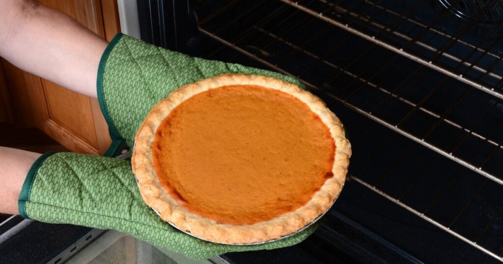 holding hot pumpkin pie with oven mitts