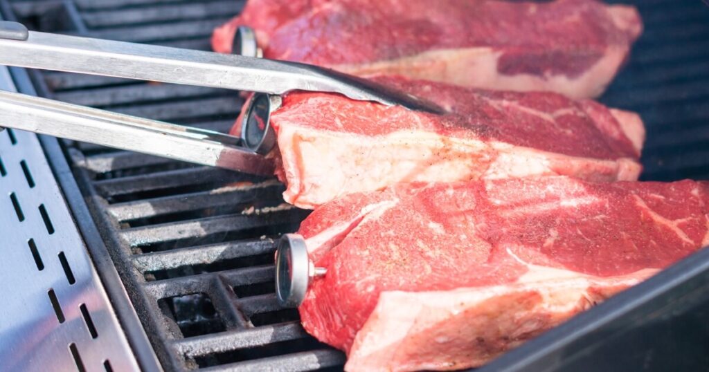 placing raw steaks on grill